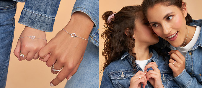 Twee personen dragen fijne gouden sieraden met hartmotief: armbanden en ringen aan de handen, evenals kettingen en oorbellen gecombineerd met spijkerjacks tegen een warme, neutrale achtergrond.