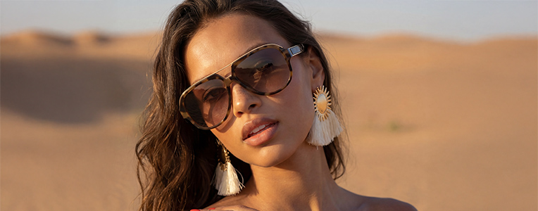 Unas gafas de sol y pendientes llamativos se presentan con estilo en una persona en un cálido paisaje desértico.