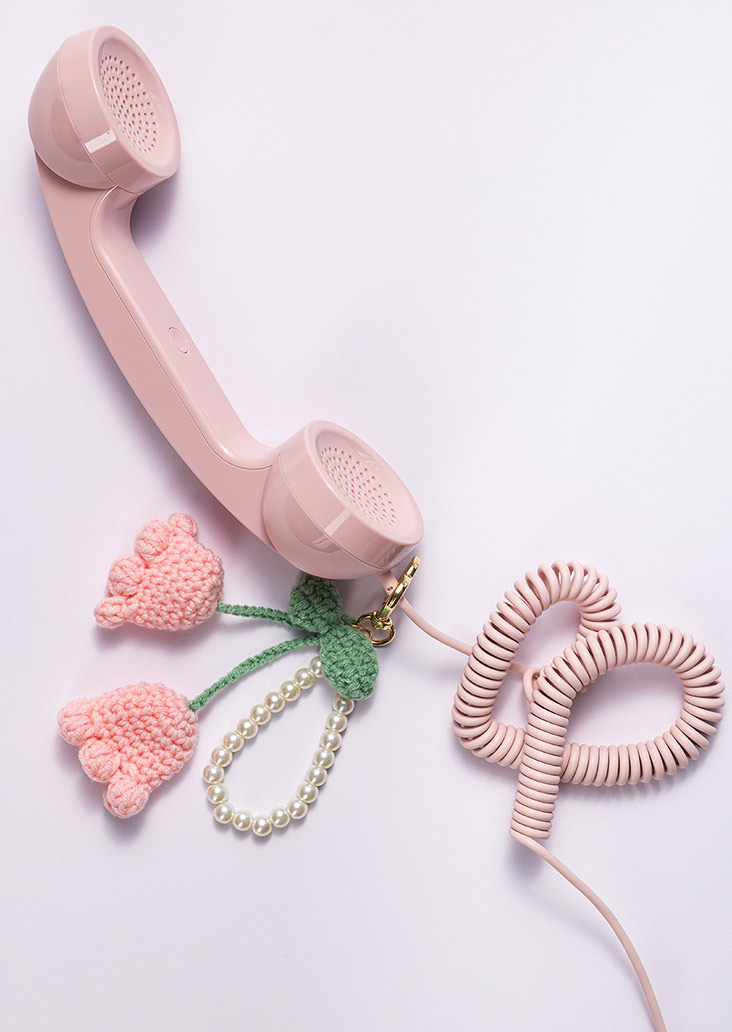 Een roze snoertelefoon met een gehaakte hanger in de vorm van twee tulpen hangt naast een witte parelarmband.