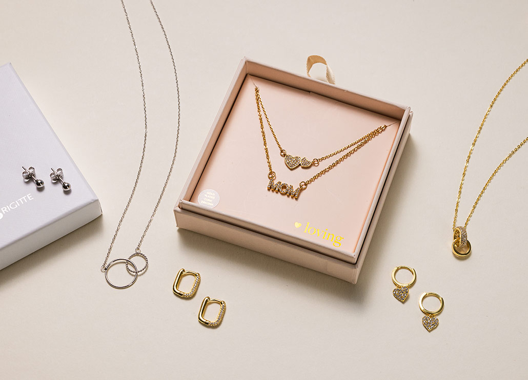 Op elkaar afgestemde sieradensets met kettingen en oorbellen in goud- en zilvertinten op een lichte ondergrond.