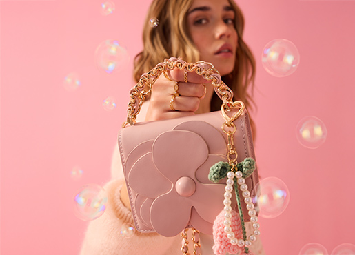 Kobieta trzyma przed kamerą różową torebkę.