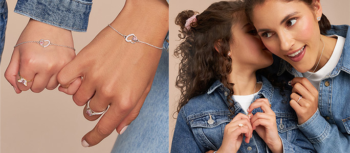 Twee personen dragen fijne gouden sieraden met hartmotief: armbanden en ringen aan de handen, evenals kettingen en oorbellen gecombineerd met spijkerjacks tegen een warme, neutrale achtergrond.