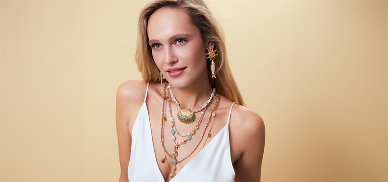 Mehrlagige Goldketten mit pastellfarbenen Details setzen einen eleganten Akzent.