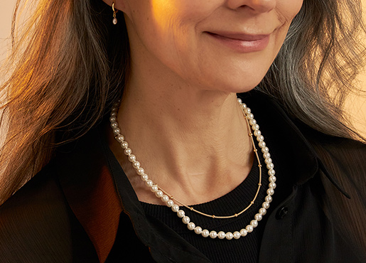 Elegante parelketting gecombineerd met een fijne gouden ketting op een donker kledingstuk.