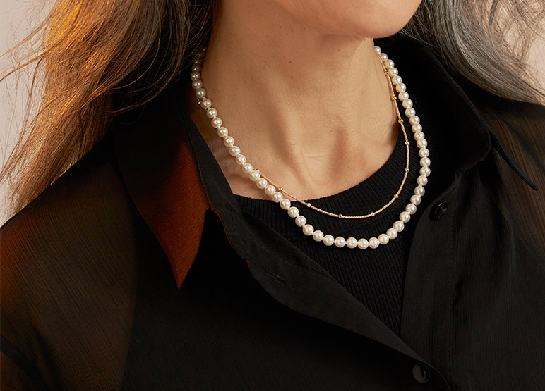 Elegante parelketting gecombineerd met een fijne gouden ketting op een donker kledingstuk.