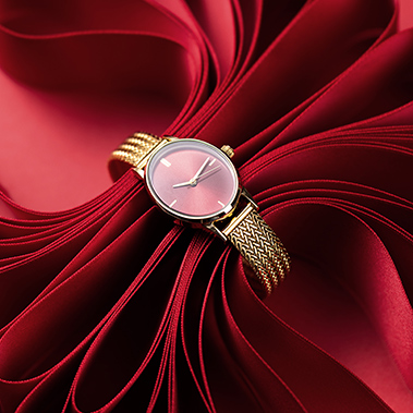 Eine goldfarbene Armbanduhr umfasst rotes Schleifenband