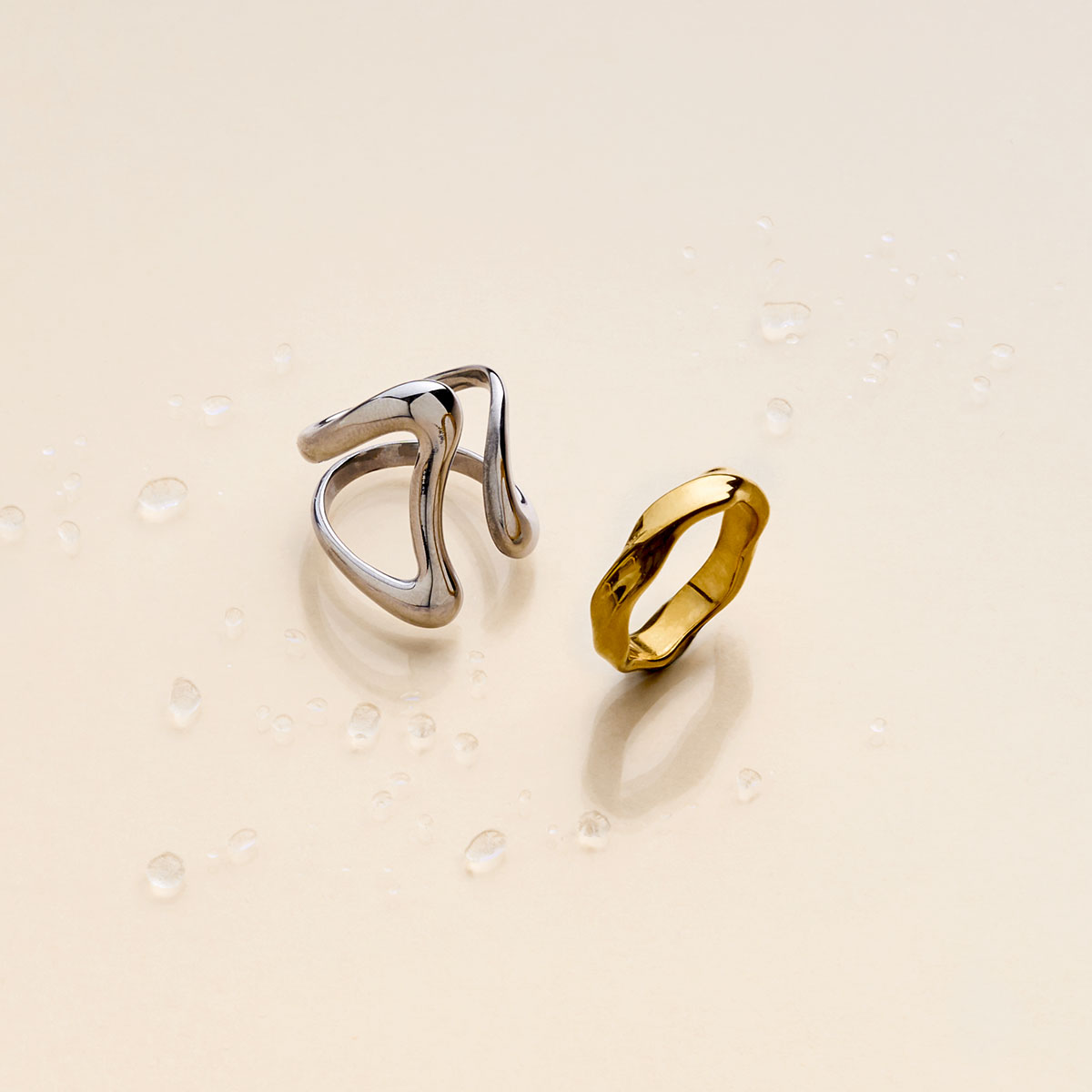 Anillos de acero inoxidable sobre un fondo beige con gotas de agua.