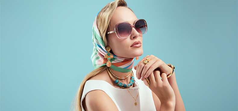 Goldene Ringe, Armbänder und türkisfarbene Ketten verleihen dem Look einen eleganten Retro‑Riviera‑Akzent.