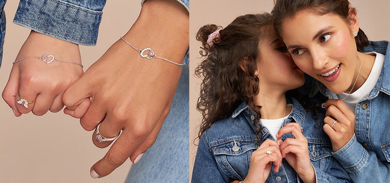 Twee personen dragen fijne gouden sieraden met hartmotief: armbanden en ringen aan de handen, evenals kettingen en oorbellen gecombineerd met spijkerjacks tegen een warme, neutrale achtergrond.