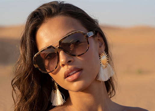Unas gafas de sol y pendientes llamativos se presentan con estilo en una persona en un cálido paisaje desértico.