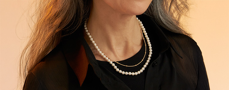 Elegante parelketting gecombineerd met een fijne gouden ketting op een donker kledingstuk.