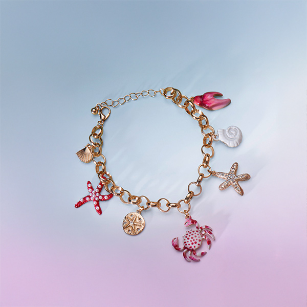 Ein goldfarbenes Charm-Armband mit Anhängern in Form von Seesternen, Muscheln, einer Krabbe und einer Blüte verleiht jedem Look eine verspielte maritime Note.