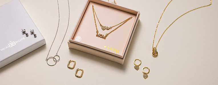 Op elkaar afgestemde sieradensets met kettingen en oorbellen in goud- en zilvertinten op een lichte ondergrond.