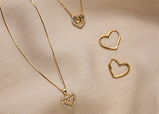 Fijne gouden sieraden met hartjeshanger en bijpassende oorbellen op lichte stof.