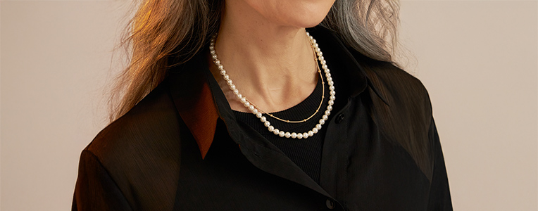 Elegante parelketting gecombineerd met een fijne gouden ketting op een donker kledingstuk.