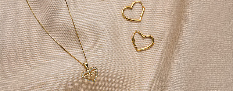 Fijne gouden sieraden met hartjeshanger en bijpassende oorbellen op lichte stof.